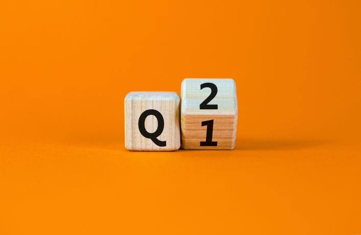 Zwei Holzblöcke auf orangefarbenem Hintergrund zeigen deutlich den Buchstaben „Q“ auf dem ersten Block und die Zahl „2“ auf dem zweiten, was subtil auf den bemerkenswerten Anstieg von Bitcoin im zweiten Quartal hinweist.