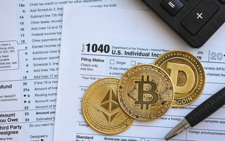 Kryptowährungsmünzen liegen auf dem US-Formular 1040. Daneben liegen ein Stift und ein Taschenrechner, was die Komplexität der Krypto-Besteuerung verdeutlicht.