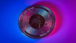Eine Cardano (ADA)-Münze auf einem Farbverlaufshintergrund mit blauer und rosa Beleuchtung, mit dem Cardano-Logo