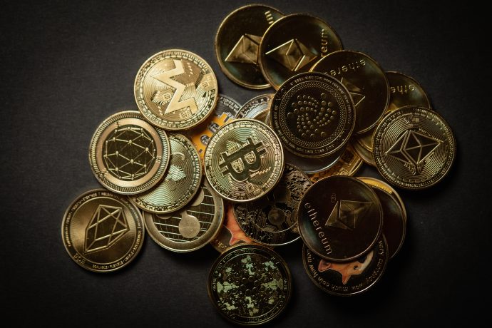 Ein Stapel verschiedener physischer Münzen, die verschiedene Kryptowährungen darstellen, darunter Bitcoin, Ethereum, Monero und IOTA, angeordnet auf einer dunklen Oberfläche.