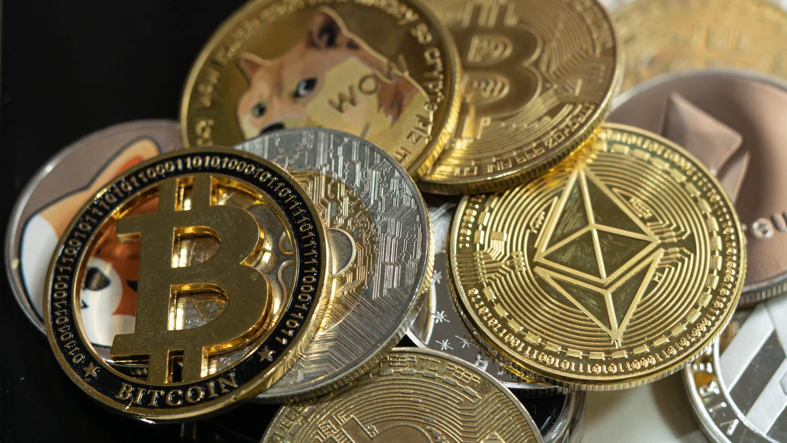 Mehrere verschiedene Kryptowährungen, darunter Bitcoin, Ethereum und Dogecoin, sind auf einer dunklen Oberfläche verstreut.