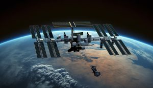 Die Internationale Raumstation umkreist die Erde, während sich ein kleineres Raumschiff nähert, vor einer atemberaubenden Kulisse aus Wolken und Kontinenten.