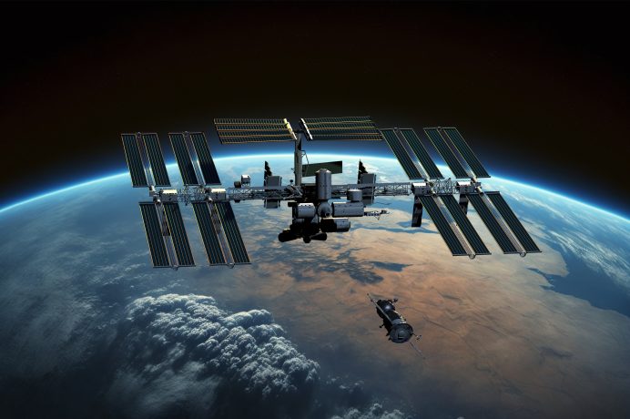 Die Internationale Raumstation umkreist die Erde, während sich ein kleineres Raumschiff nähert, vor einer atemberaubenden Kulisse aus Wolken und Kontinenten.