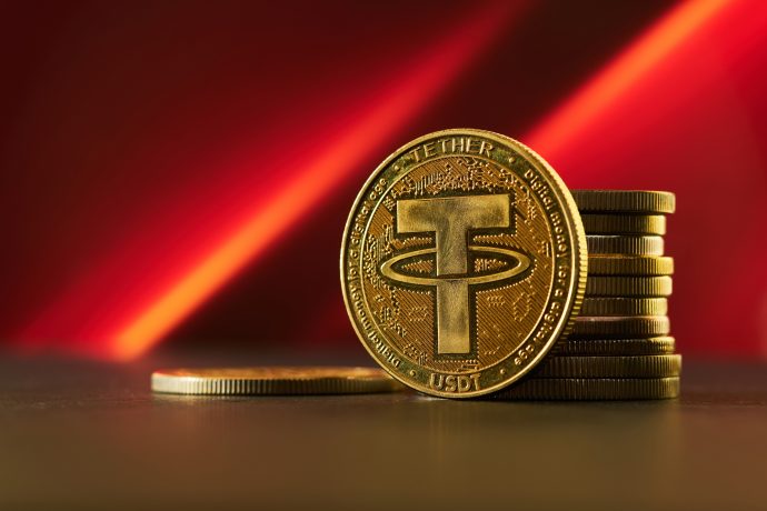 Ein Stapel goldfarbener Münzen mit einer auffälligen Münze auf der Vorderseite mit dem Tether-Logo vor einem roten Hintergrund symbolisiert die Stärke der Stablecoin auf dem Kryptowährungsmarkt.