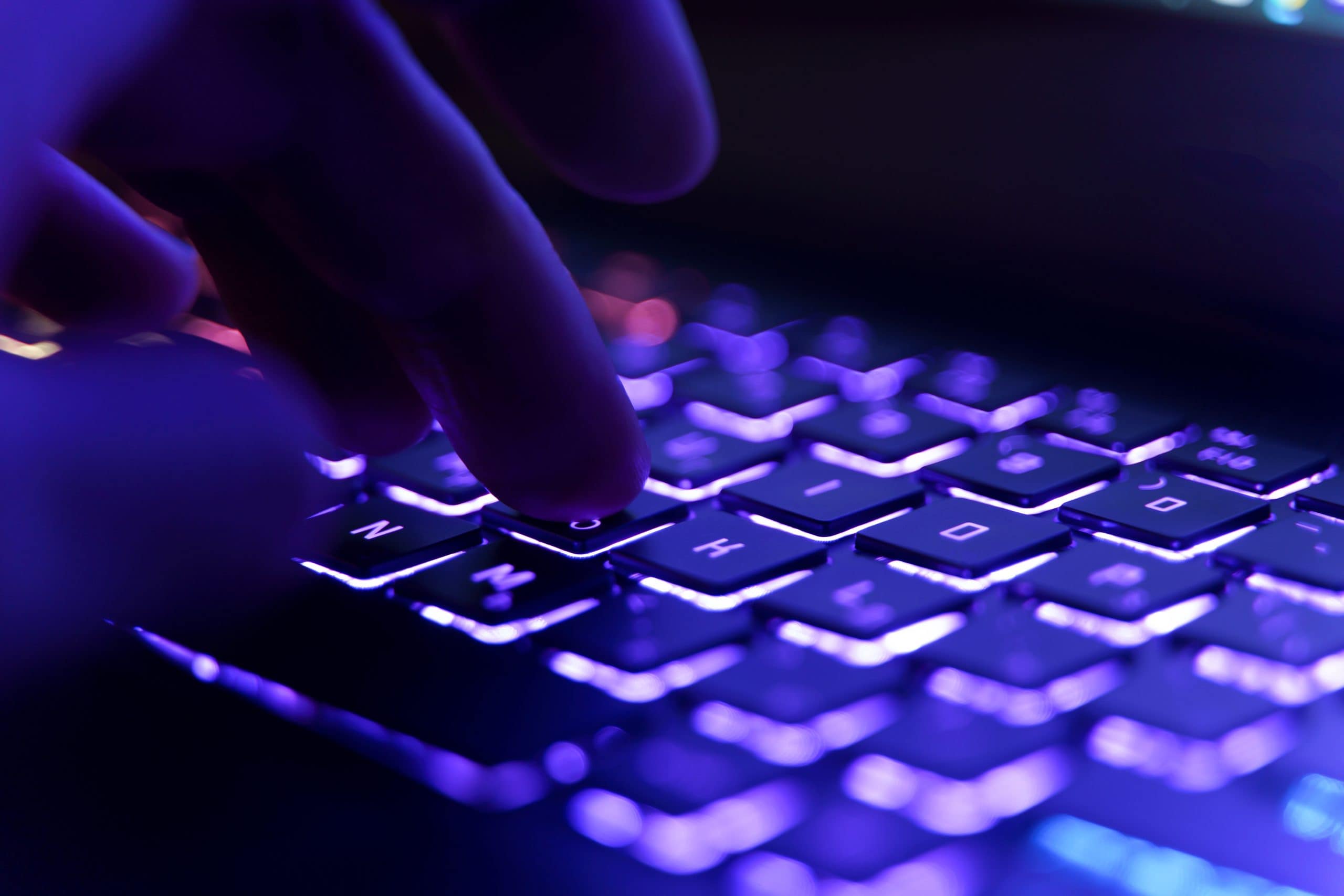 Finger tippen auf einer Tastatur mit Hintergrundbeleuchtung und violetter Beleuchtung