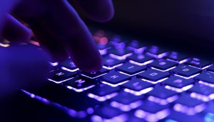 Finger tippen auf einer hintergrundbeleuchteten Tastatur mit violetter und blauer Beleuchtung.