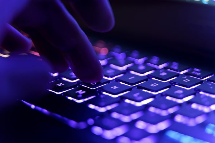 Finger tippen auf einer hintergrundbeleuchteten Tastatur mit violetter und blauer Beleuchtung.