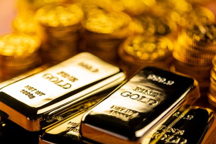 Verschiedene Goldbarren sind vor einem Haufen Goldmünzen zu sehen.
