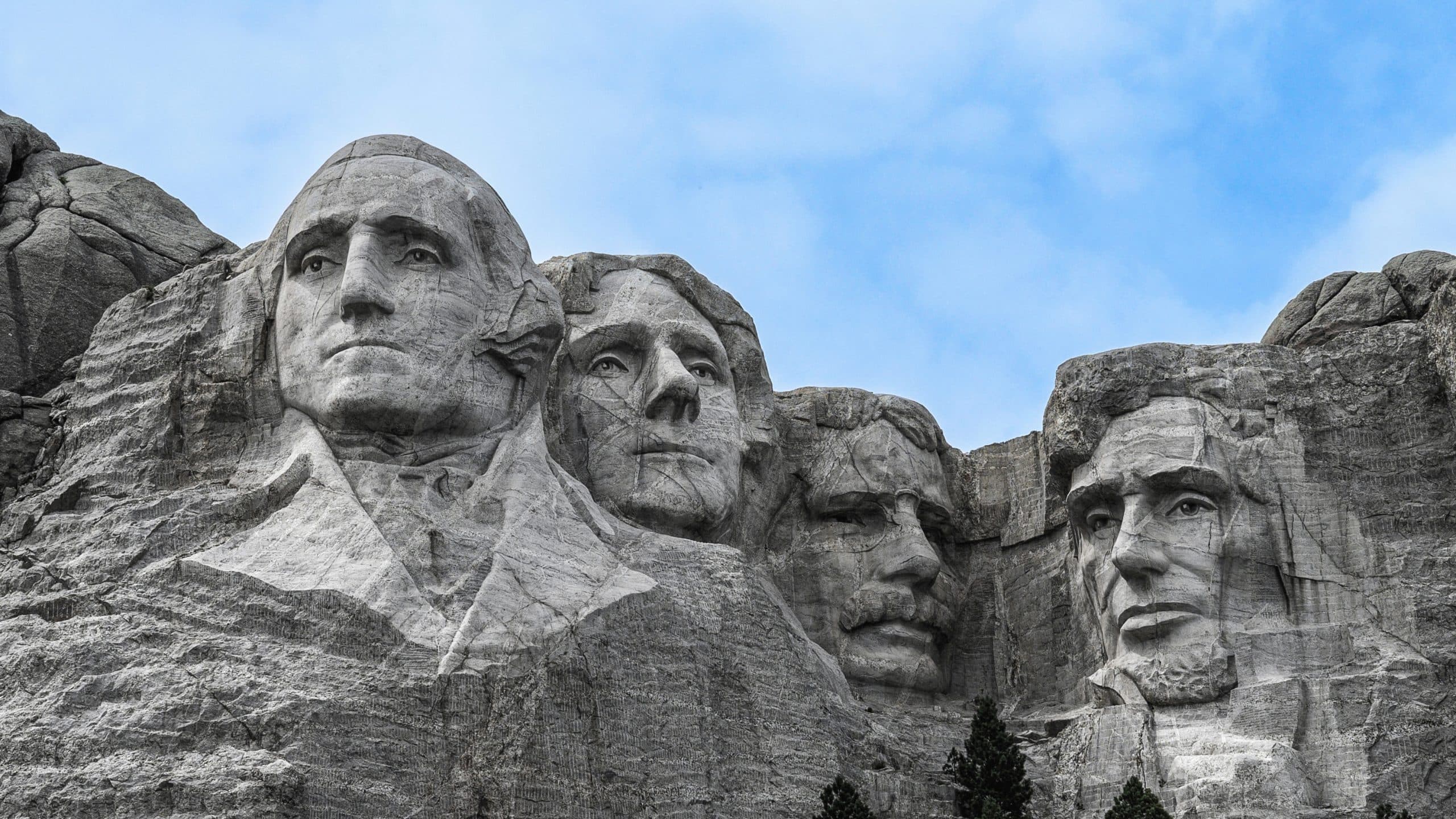 Das Mount Rushmore National Memorial zeigt die eingemeißelten Gesichter von US-Präsidenten vor dem Hintergrund eines bewölkten blauen Himmels.