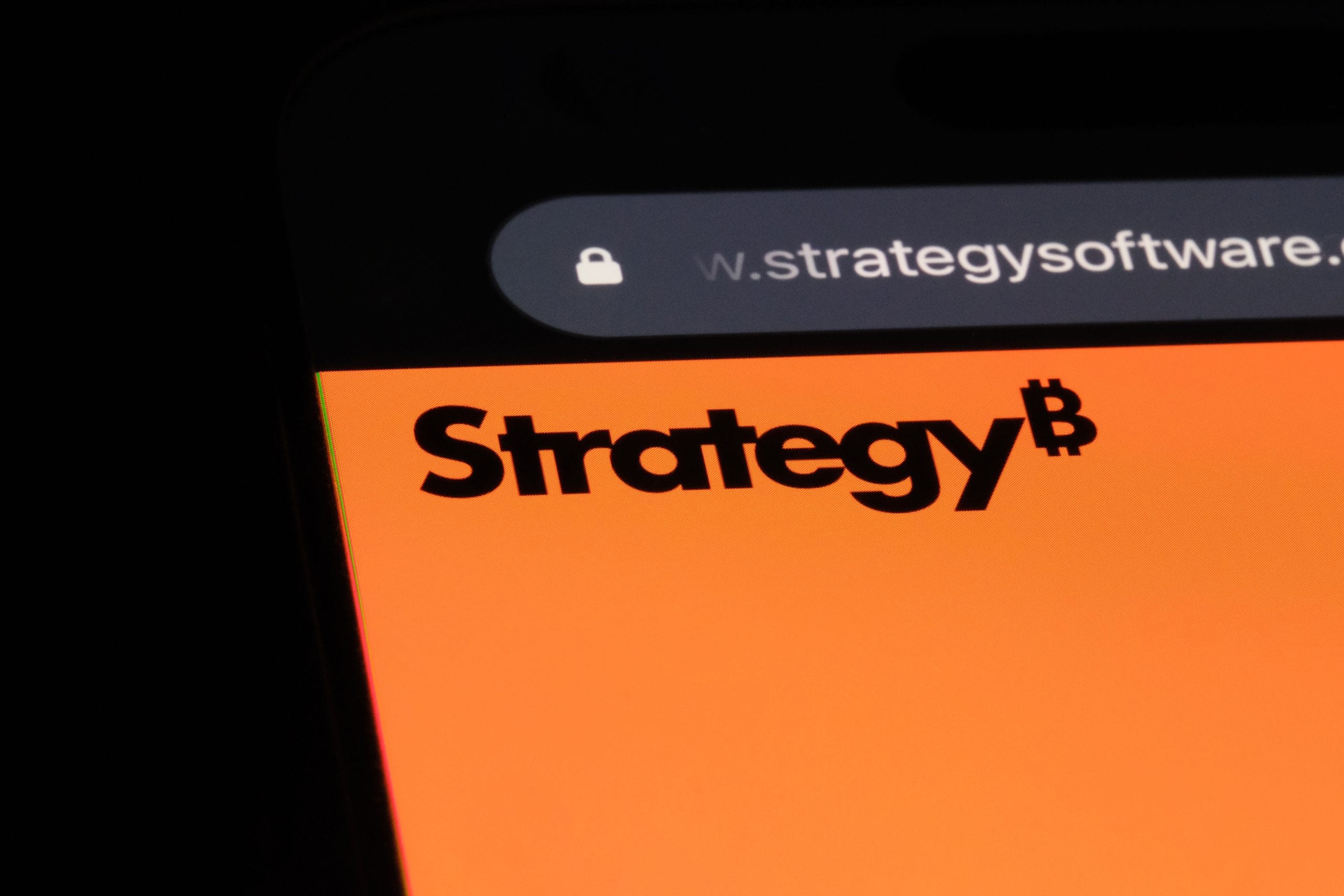 Eine Nahaufnahme eines Smartphone-Bildschirms zeigt eine leuchtend orangefarbene Webseite mit dem Wort „Strategie“ neben einem Bitcoin-Symbol, was auf finanzielle Einblicke hindeutet. In der Adressleiste des Browsers schimmert eine teilweise URL durch und verspricht Spannung und Entdeckungen.