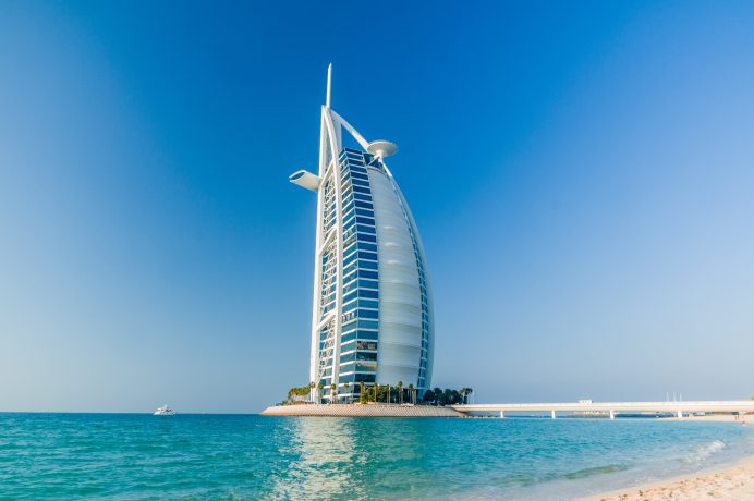 Ein großes, segelförmiges Luxushotel auf einer kleinen Insel, umgeben vom Meer unter einem klaren blauen Himmel, das die Eleganz und Innovation von Solana widerspiegelt.