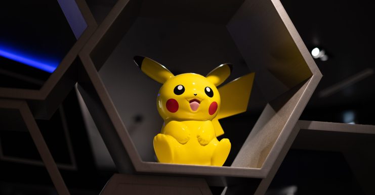 Eine gelbe Pikachu-Figur steht in einem sechseckigen Ausstellungsregal mit dunklem Hintergrund und verleiht der Szene einen Hauch von Sui-inspiriertem Charme.