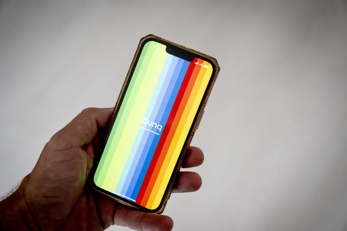 Eine Hand hält ein Smartphone mit vertikalen Regenbogenstreifen und dem Wort „bunq“ in der Mitte, wodurch das farbenfrohe Branding der Bunq-Banking-App hervorgehoben wird.