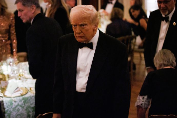 Donald Trump im schwarzen Smoking steht in einem formellen Veranstaltungsrahmen, umgeben von anderen Gästen, während die Atmosphäre von lebhaften Diskussionen und Meinungs-ECHO unter den Teilnehmern geprägt ist.