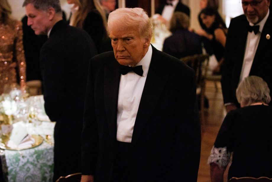 Donald Trump im schwarzen Smoking steht in einem formellen Veranstaltungsrahmen, umgeben von anderen Gästen, während die Atmosphäre von lebhaften Diskussionen und Meinungs-ECHO unter den Teilnehmern geprägt ist.
