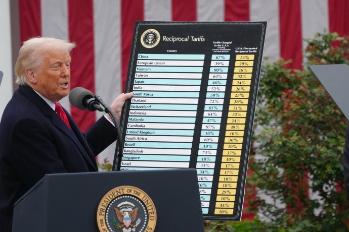 Donald Trump hält ein Schild in der Hand, auf dem die Zoll-Tarife abgebildet sind