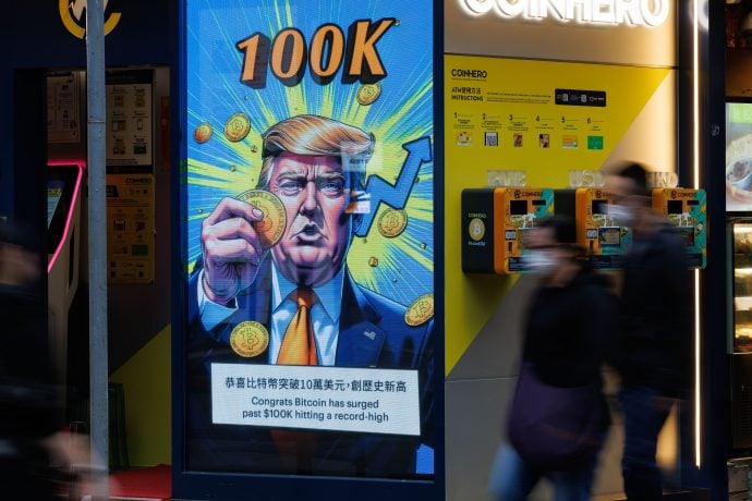 Eine digitale Anzeige zeigt eine stilisierte Cartoonfigur mit Bitcoin-Münzen, die den 100.000-Dollar-Wert der Kryptowährung feiert. Für Passanten auf der Straße gleicht die Szene einem automatisch gespeicherten Entwurf einer neuen Finanzära.