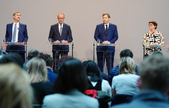 Vier Männer und eine Frau stehen während einer Podiumsdiskussion über Krypto-Regulierungen an Podien und blicken auf ein aufmerksames Publikum.