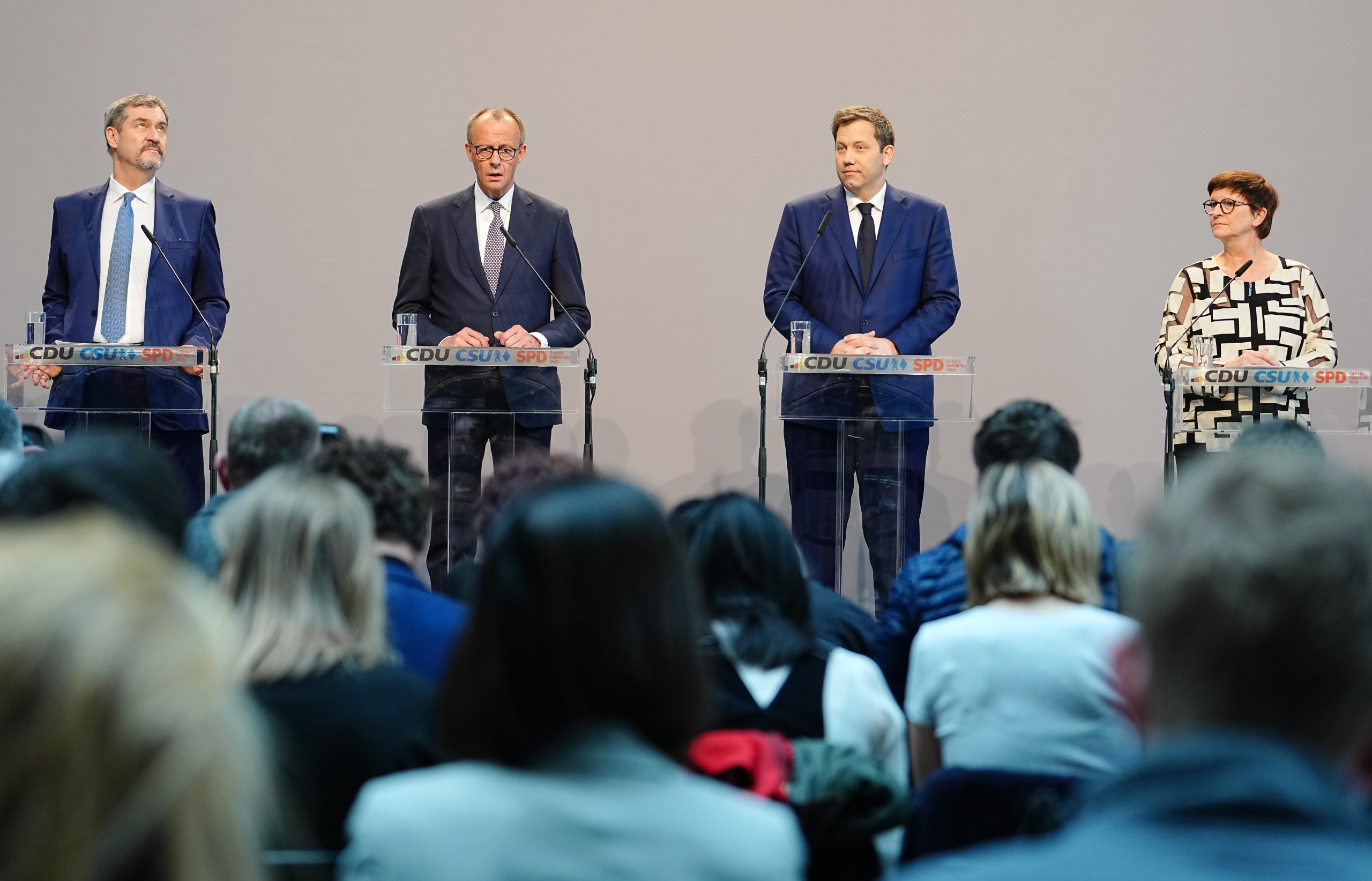 Vier Männer und eine Frau stehen während einer Podiumsdiskussion über Krypto-Regulierungen an Podien und blicken auf ein aufmerksames Publikum.