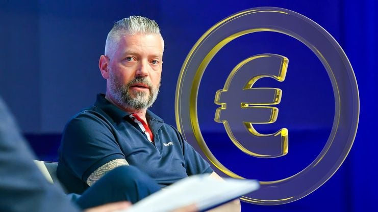 AllUnity-CEO Alex Höptner sitzt auf einer Bühne vor einem Euro-Symbol