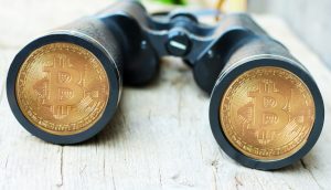 Ein Fernglas mit Bitcoin-Münzen auf den Linsen auf einer Holzoberfläche.