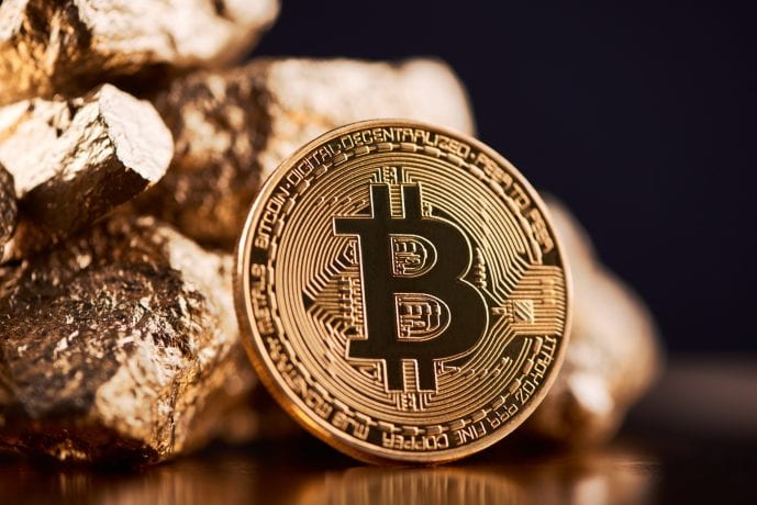 Eine physische Darstellung eines Bitcoins steht stolz neben einem Haufen schimmernder Goldnuggets und unterstreicht den Wert der digitalen Währung im Vergleich zu traditionellen Goldreserven.