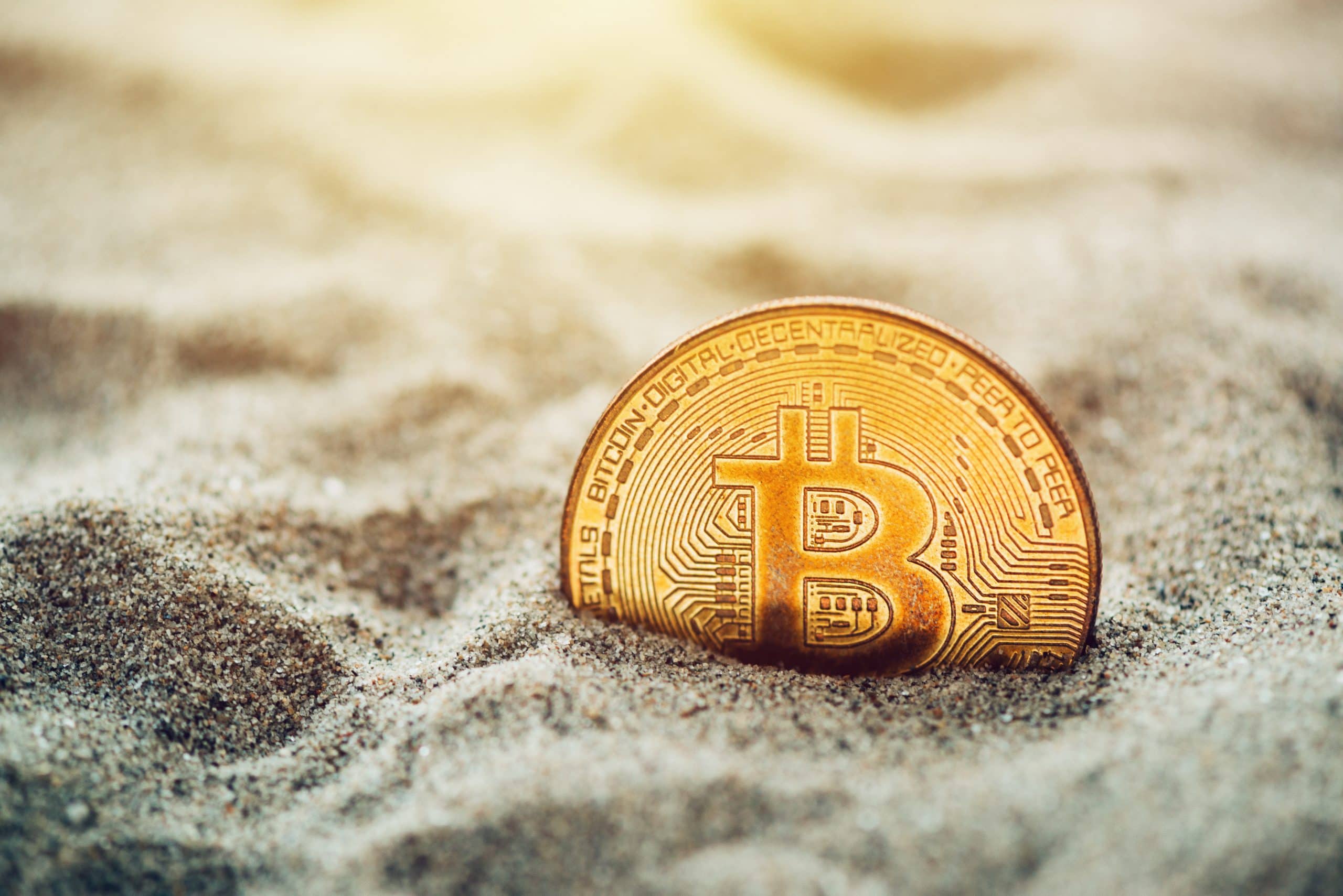 Ein goldfarbener Bitcoin, teilweise im Sand vergraben, mit Sonnenlicht, das den Hintergrund beleuchtet – ein passendes Bild für Krypto-Anleger, die von einer Steuerwüste träumen oder über das Auswandern nachdenken.