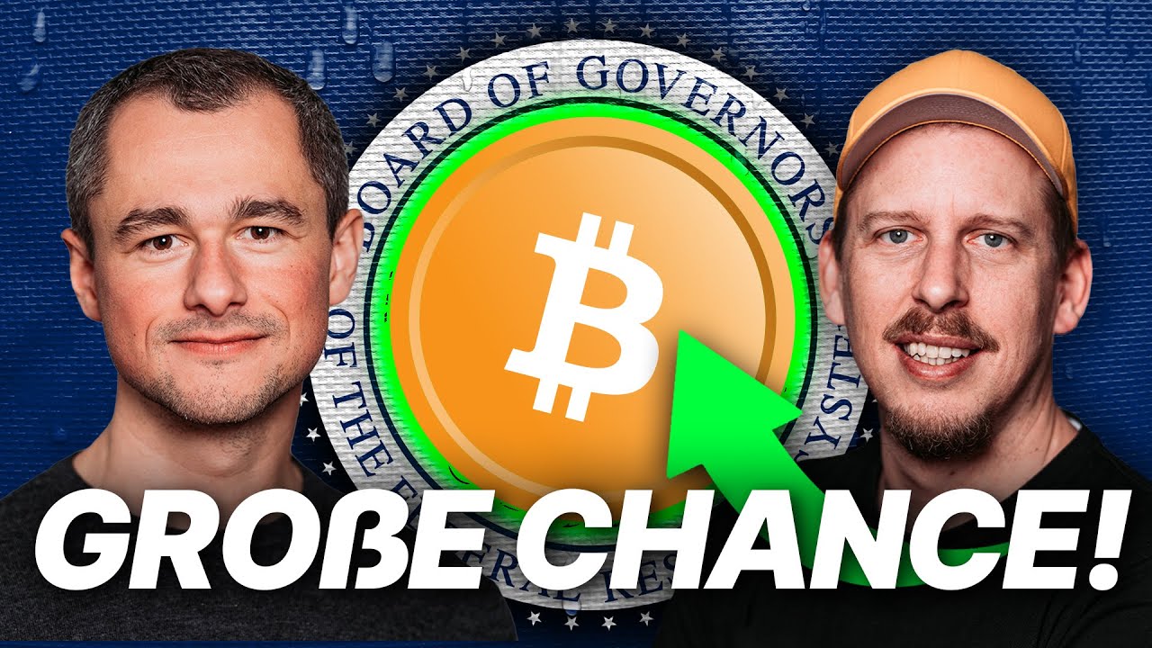 Zwei Männer stehen auf beiden Seiten eines großen Bitcoin-Symbols, auf das ein grüner Pfeil zeigt und darunter der deutsche Text „GROßE CHANCE!“ angezeigt wird, der auf mögliche Auswirkungen der US-Notenbank hinweist.