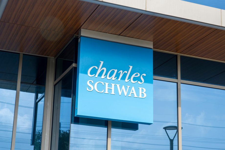 An der Außenseite eines modernen Glasgebäudes ist ein blaues Schild mit der weißen Aufschrift „Charles Schwab“ angebracht.
