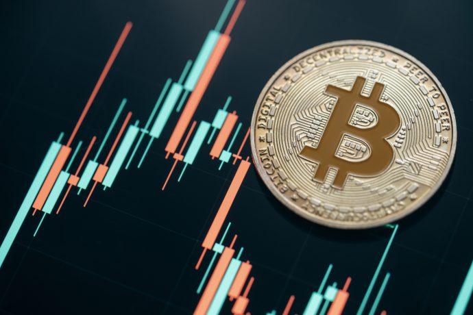 Eine Bitcoin-Münze liegt auf einer Oberfläche vor dem Hintergrund eines Finanz-Candlestick-Charts, das das neueste Krypto-Marktupdate widerspiegelt und aktuelle Markttrends signalisiert.