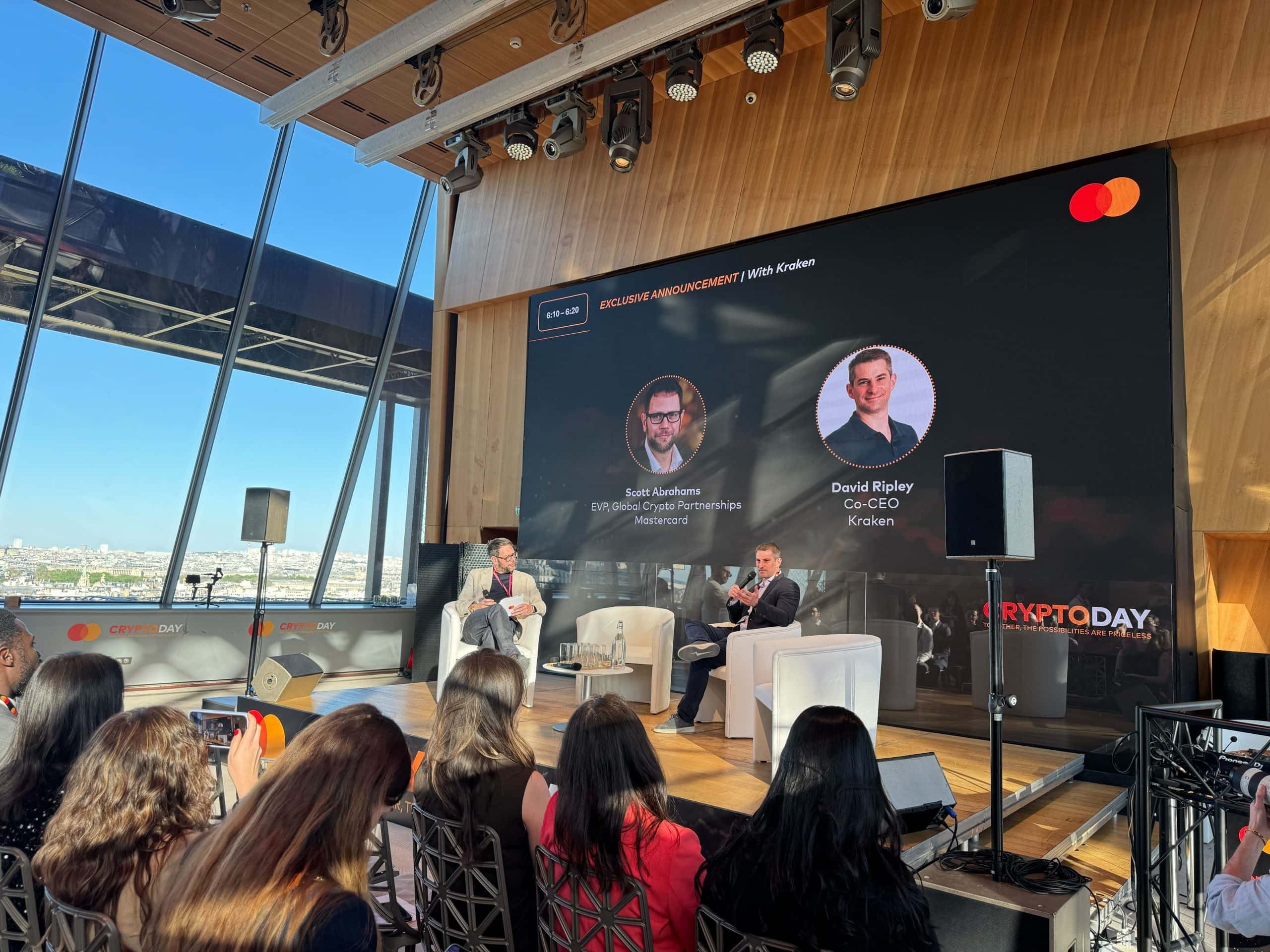 Eine Podiumsdiskussion mit Entwurf, zwei Sprechern und einem großen digitalen Bildschirm. Die Zuschauer genießen durch große Fenster den Blick auf die Stadtlandschaft, während das Event-Branding deutlich sichtbar bleibt.