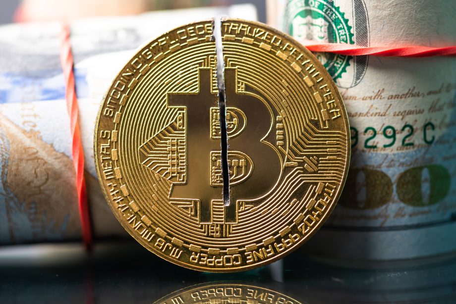 Eine in zwei Hälften geteilte goldene Bitcoin-Münze steht aufrecht vor gerollten US-Dollarscheinen, die mit roten Gummibändern zusammengehalten werden – ein Bild, das an einen automatisch gespeicherten Entwurf der Finanztransformation erinnert.