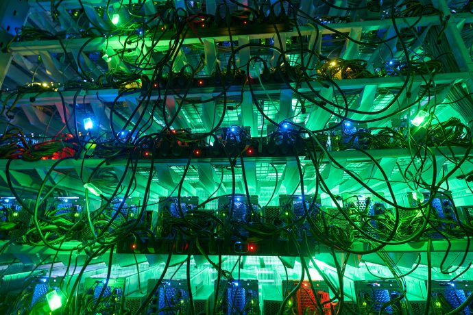 Ein dichtes Netzwerk aus Kabeln und LED-Leuchten in Grün- und Blautönen verbindet die elektronischen Geräte in den Regalen, möglicherweise ein Rechenzentrum oder einen Serverraum, der Bitcoin-Transaktionen ermöglicht.