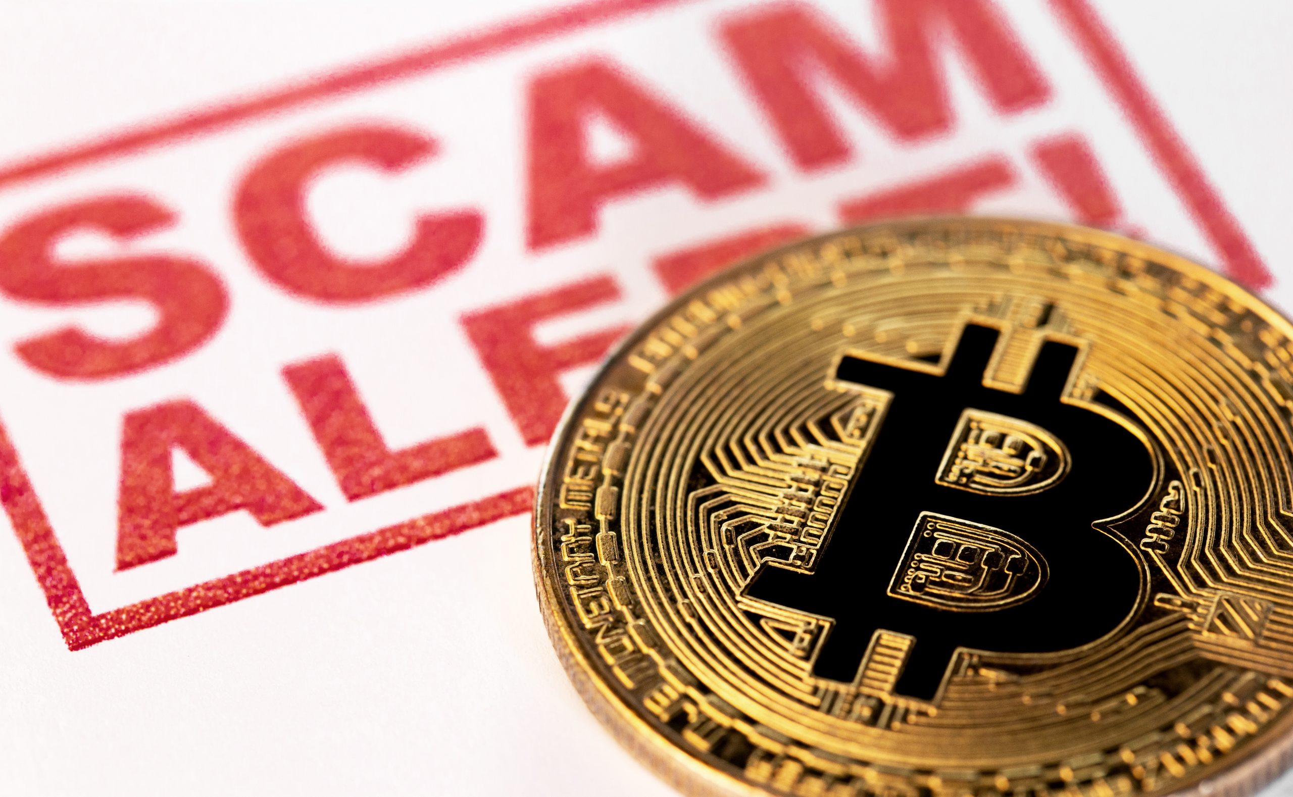 Bitcoin-Münze auf Papier mit fettem roten Text mit der Aufschrift „SCAM ALERT“, einer Warnung eines Krypto-Sicherheitsexperten vor einer Betrugsmasche auf dem Markt.