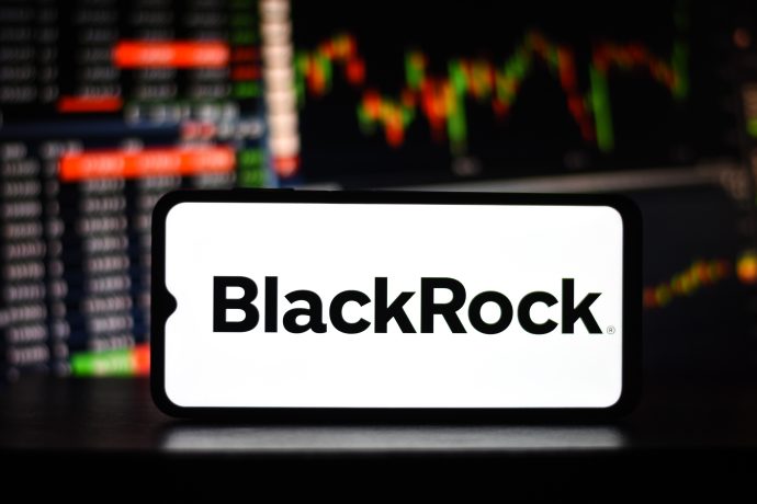 Auf einem Smartphone wird das BlackRock-Logo mit Finanzdiagrammen im Hintergrund angezeigt, was auf mögliche Trends bei Bitcoin-ETFs hindeutet.