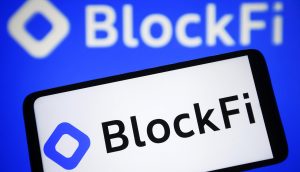 Das auf einem Smartphone-Bildschirm angezeigte BlockFi-Logo mit einer größeren Version im unscharfen Hintergrund.