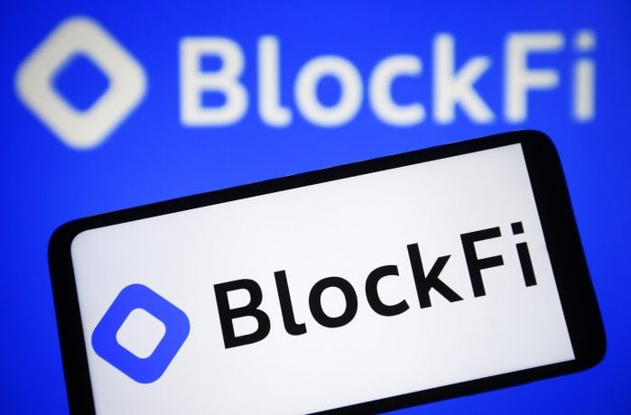 Das auf einem Smartphone-Bildschirm angezeigte BlockFi-Logo mit einer größeren Version im unscharfen Hintergrund.