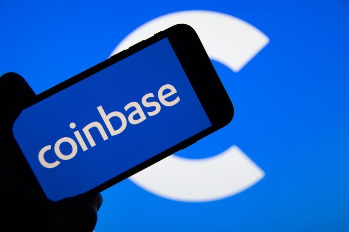 Eine Hand hält ein Smartphone mit dem Coinbase-Logo und einem großen, unscharfen Coinbase-C-Logo im Hintergrund, das die Bedeutung von Coinbase im digitalen Finanzwesen unterstreicht.
