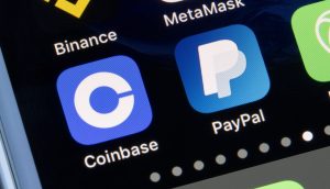 Nahaufnahme eines Smartphone-Bildschirms, auf dem neben einer Laptop-Tastatur die App-Symbole von Coinbase, PayPal, Binance, MetaMask und Crypto.com angezeigt werden.