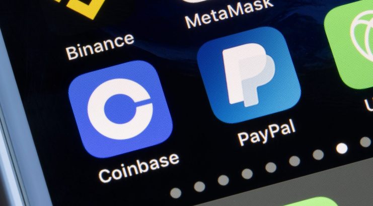 Nahaufnahme eines Smartphone-Bildschirms, auf dem neben einer Laptop-Tastatur die App-Symbole von Coinbase, PayPal, Binance, MetaMask und Crypto.com angezeigt werden.