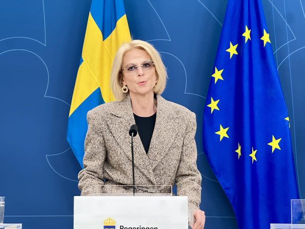 Elisabeth Svantesson spricht an einem Podium mit schwedischen und EU-Flaggen im Hintergrund.