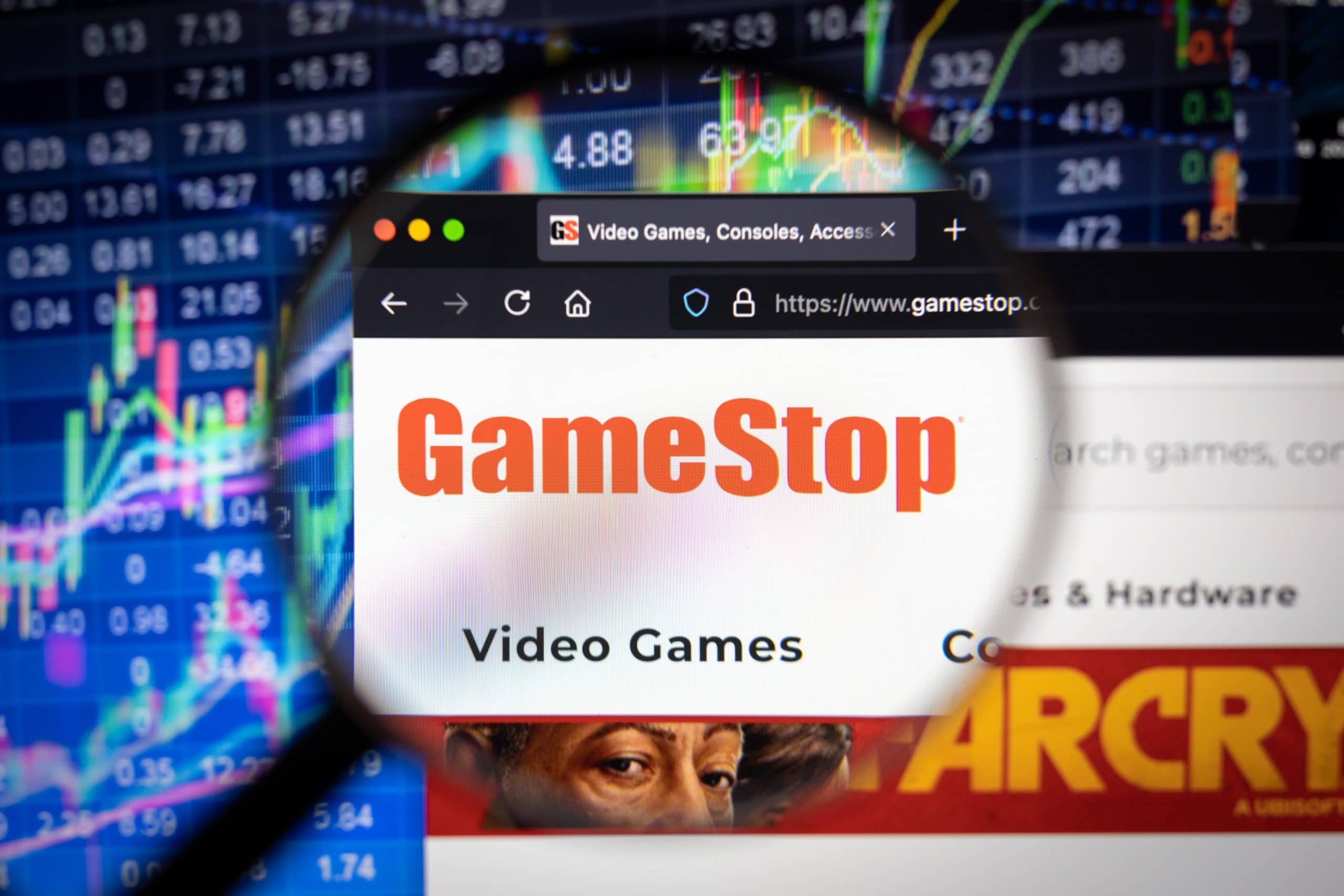 Eine Lupe fokussiert auf die GameStop-Website, die auf einem Computerbildschirm angezeigt wird, vor dem Hintergrund dynamischer Börsendiagramme und -charts.