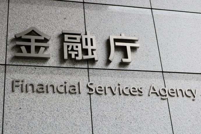 Ein Schild an einem Gebäude zeigt japanischen Text über „Financial Services Agency“ auf Englisch vor einem grau gekachelten Hintergrund. Dies spiegelt Japans zentrale Rolle im globalen Finanzwesen wider, wo traditionelle Dienstleistungen auf moderne Innovationen wie Krypto-Finanzprodukte treffen.