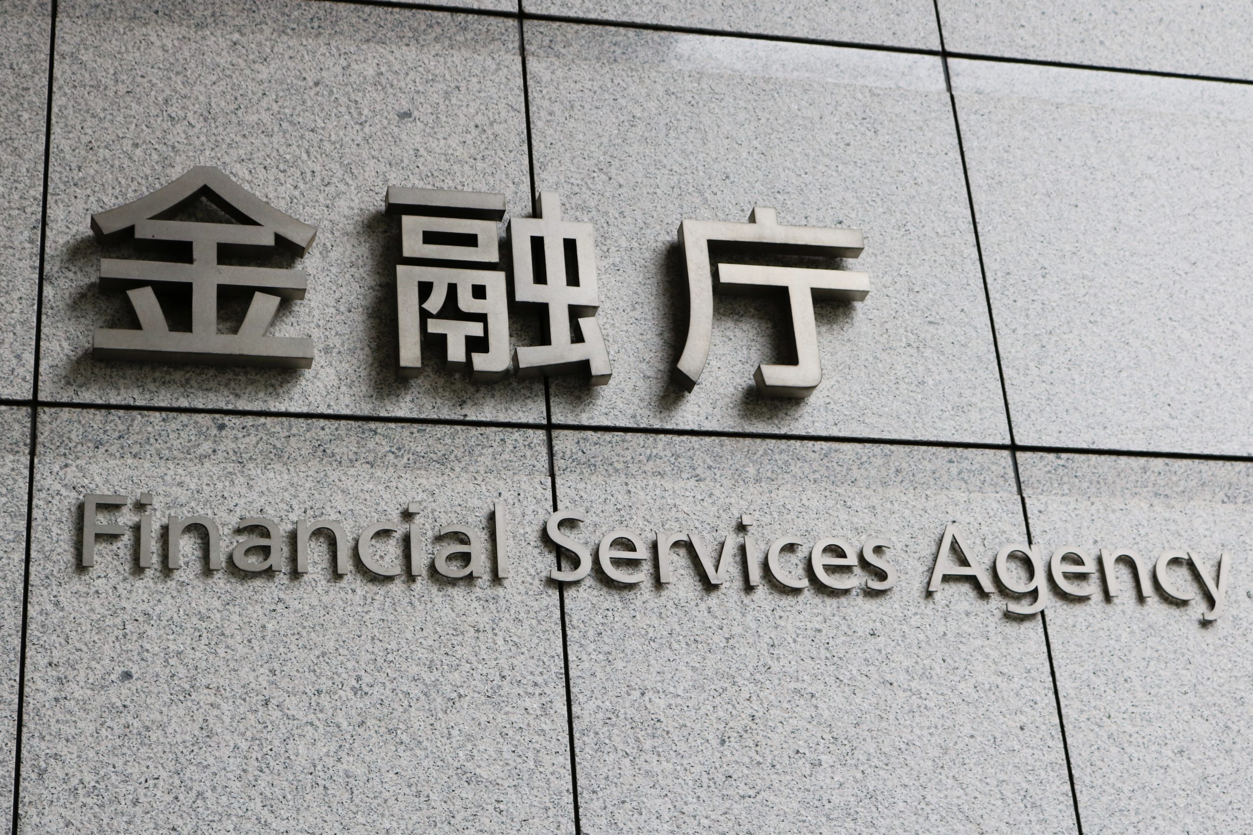 Ein Schild an einem Gebäude zeigt japanischen Text über „Financial Services Agency“ auf Englisch vor einem grau gekachelten Hintergrund. Dies spiegelt Japans zentrale Rolle im globalen Finanzwesen wider, wo traditionelle Dienstleistungen auf moderne Innovationen wie Krypto-Finanzprodukte treffen.