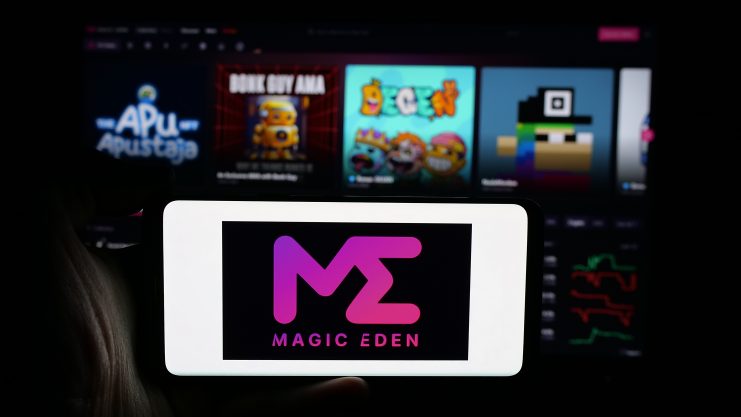 Ein Smartphone mit dem Magic Eden-Logo wird vor einem lebendigen, unscharfen Hintergrund mit bunten App-Symbolen auf dem Bildschirm gehalten, was seine Rolle als führender NFT-Marktplatz hervorhebt.