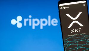 Auf einem Smartphone wird das Ripple-XRP-Logo mit dem Text „The Digital Asset for Payments“ vor einem leicht verschwommenen Ripple-Hintergrund angezeigt.