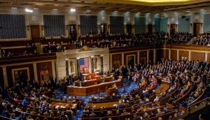 Eine große Versammlung in einem Parlamentssaal, bei der die Beamten in Reihen sitzen und die amerikanische Flagge stolz gezeigt wird, fängt den Geist der USA ein, während die Zuschauer von den oberen Galerien aus zusehen.