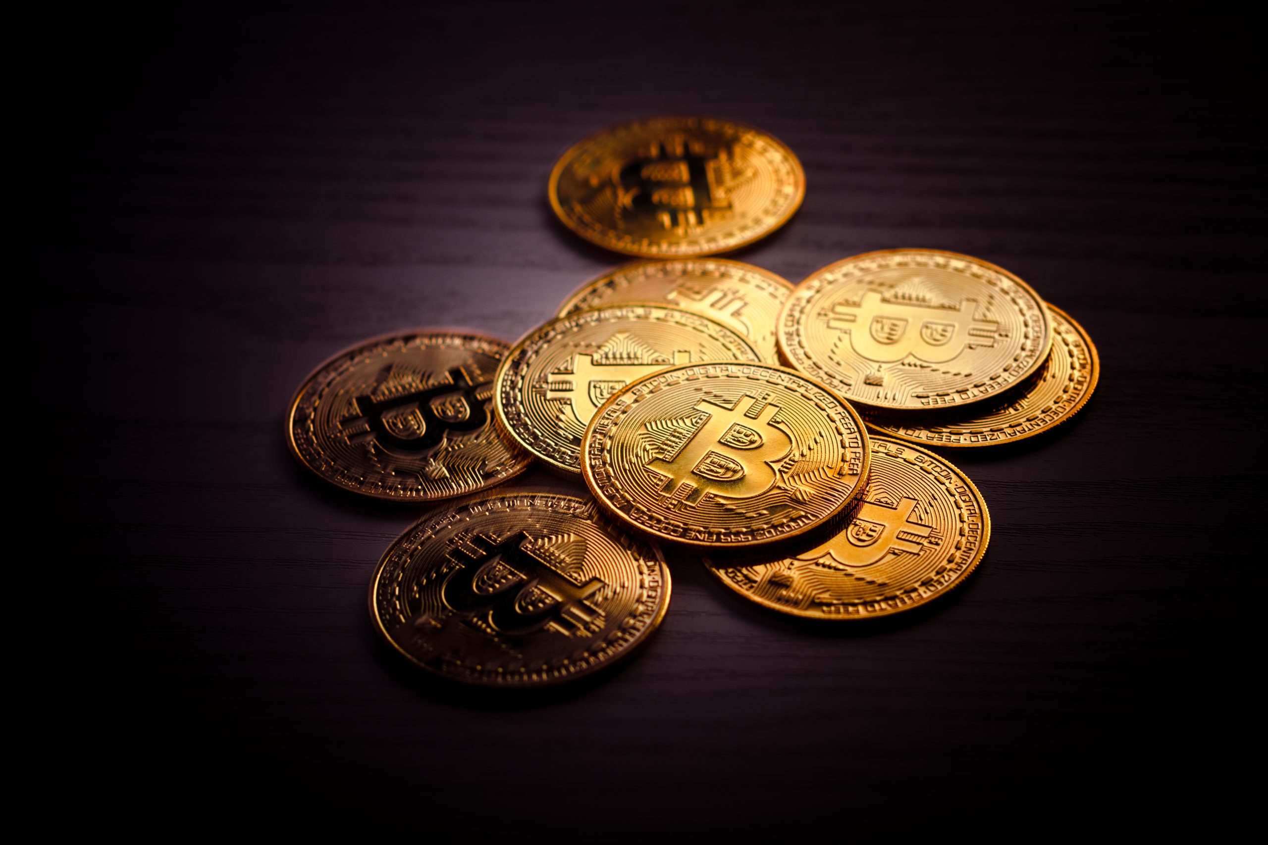 Ein Stapel goldfarbener physischer Münzen mit dem Bitcoin-Symbol wird auf einer dunklen Holzoberfläche präsentiert und hebt die greifbare Seite von Bitcoin hervor.