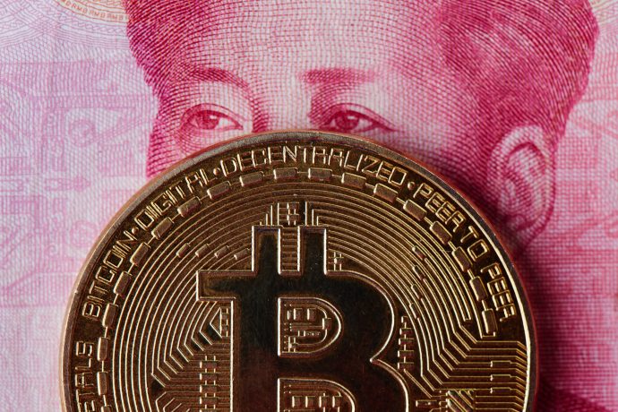 Eine Bitcoin-Münze, die vor einem Teil einer chinesischen Yuan-Banknote platziert ist und das Porträt teilweise verdeckt.
