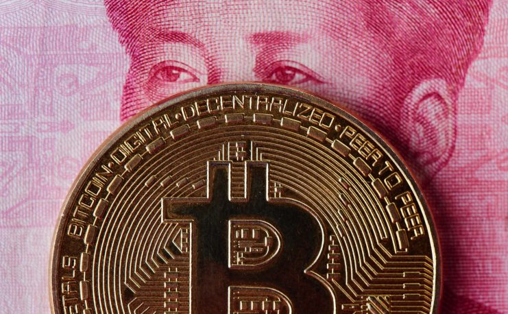 Eine Bitcoin-Münze, die vor einem Teil einer chinesischen Yuan-Banknote platziert ist und das Porträt teilweise verdeckt.